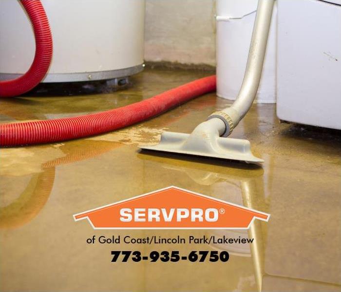 A basement floor is covered in water and a water extraction hose is leaning on the washing machine.